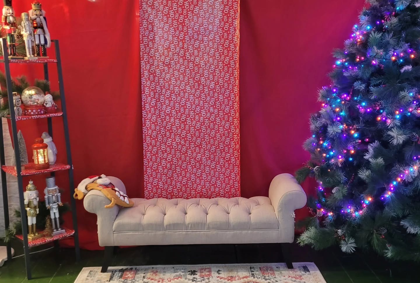 The Grotto set at Groucho’s: a red backdrop, a cream buttoned bench, nutcrackers and a lit Christmas tree